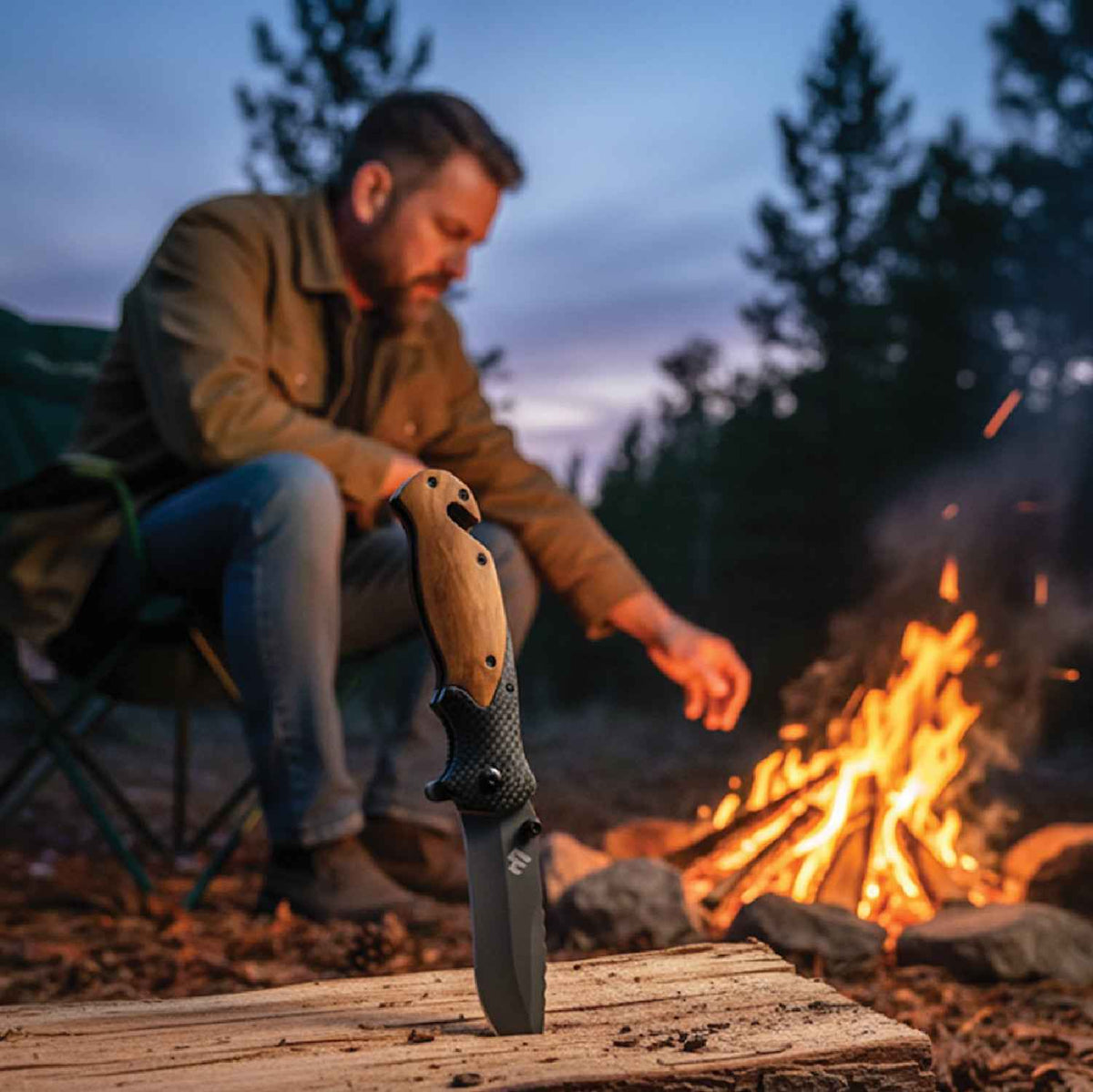 Man sitting by a campfire at dusk holding a Ridgeblade folding knife