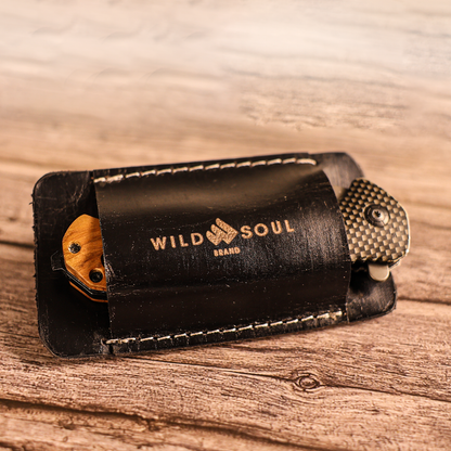 Wild Soul Brand black leather knife holster on a wood surface with a folding knife partially drawn