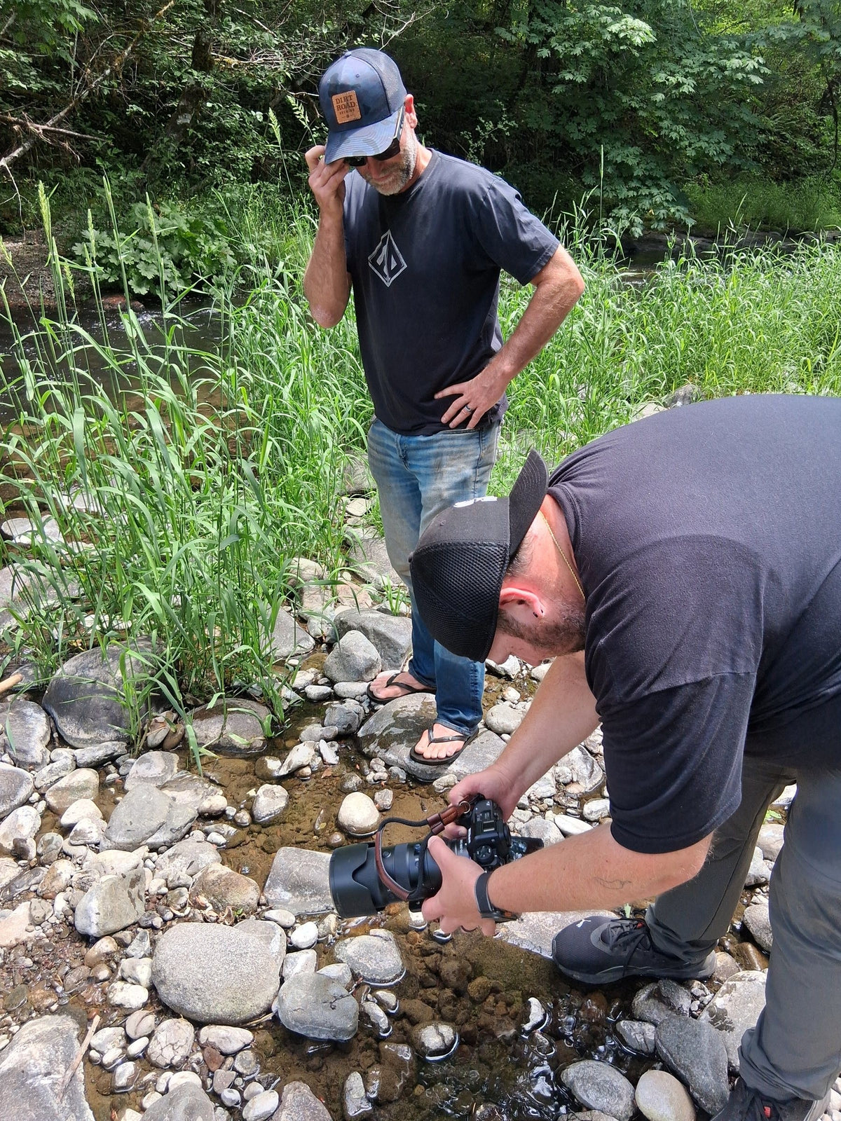 Photographer Charles Anthony crouching with a camera in a creek bed during a product photoshoot