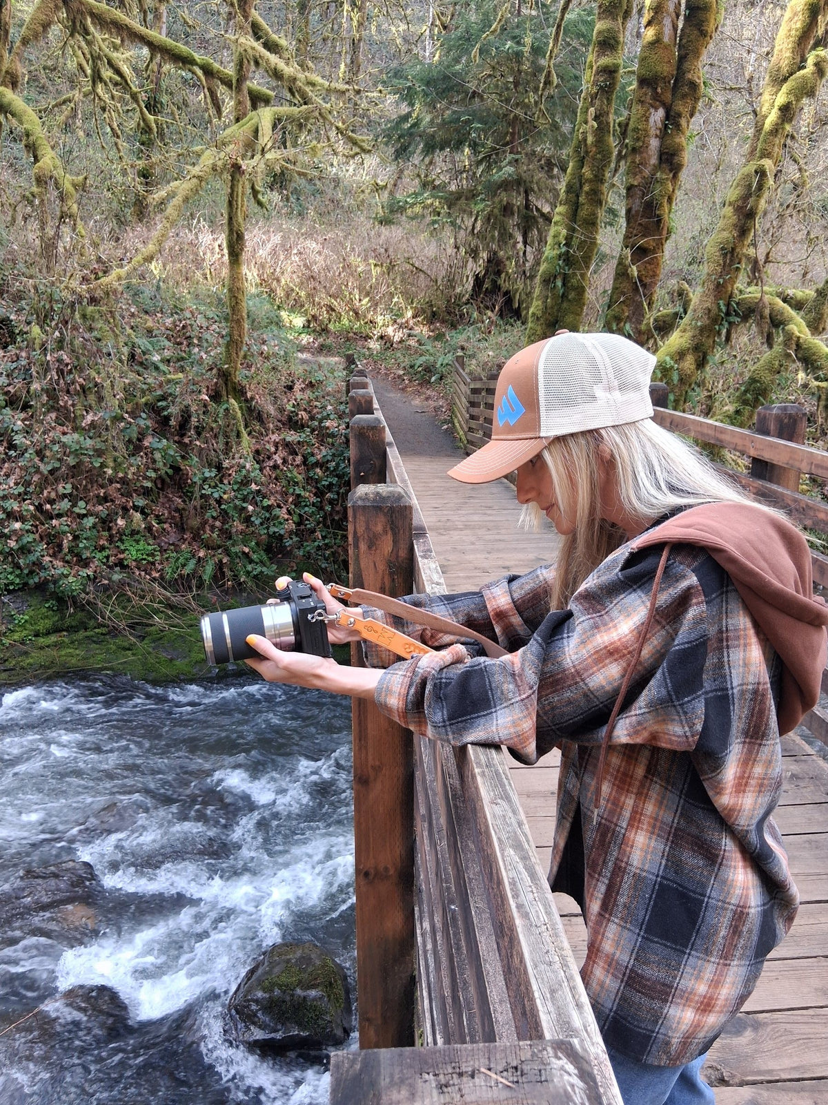 Photographer Melody Jordan photographing gear from a footbridge over a forest creek