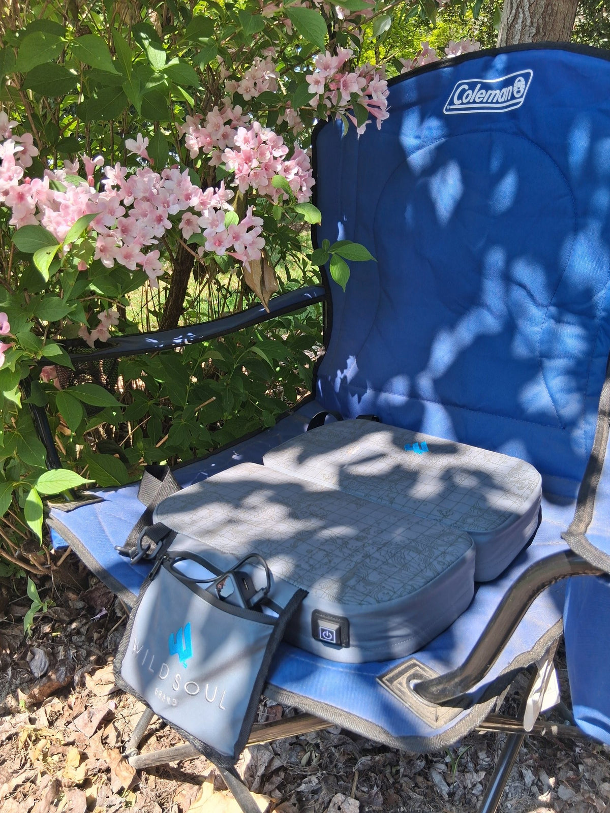 NextPad Camp seat cushion and carry bag on a folding camp chair under flowering shrubs