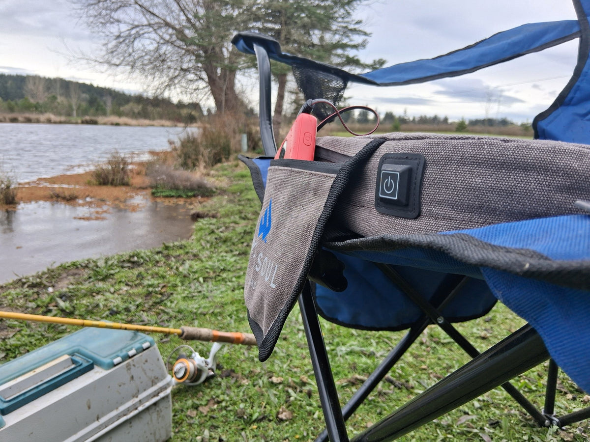 NextPad Camp heated seat cushion on a camp chair beside a lake with a fishing rod and tackle box
