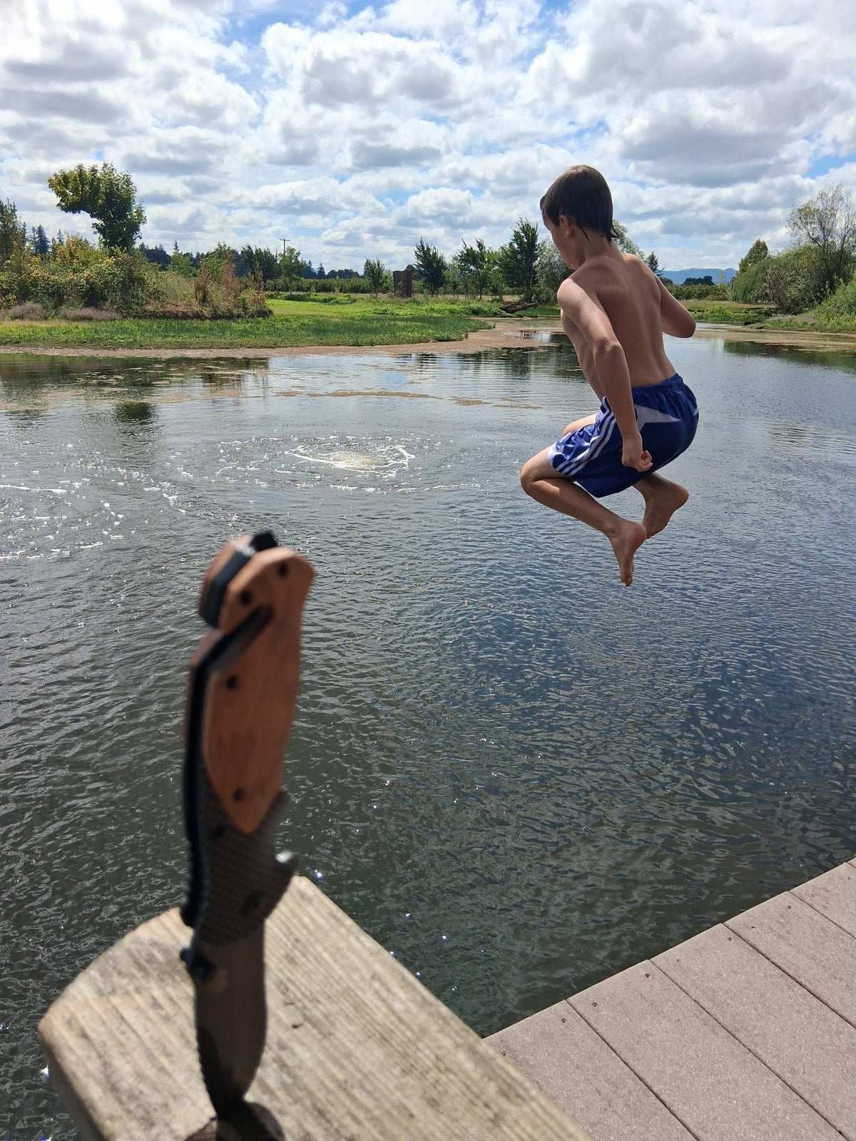 Ridgeblade folding knife stuck in a dock post while a boy jumps into the pond behind it
