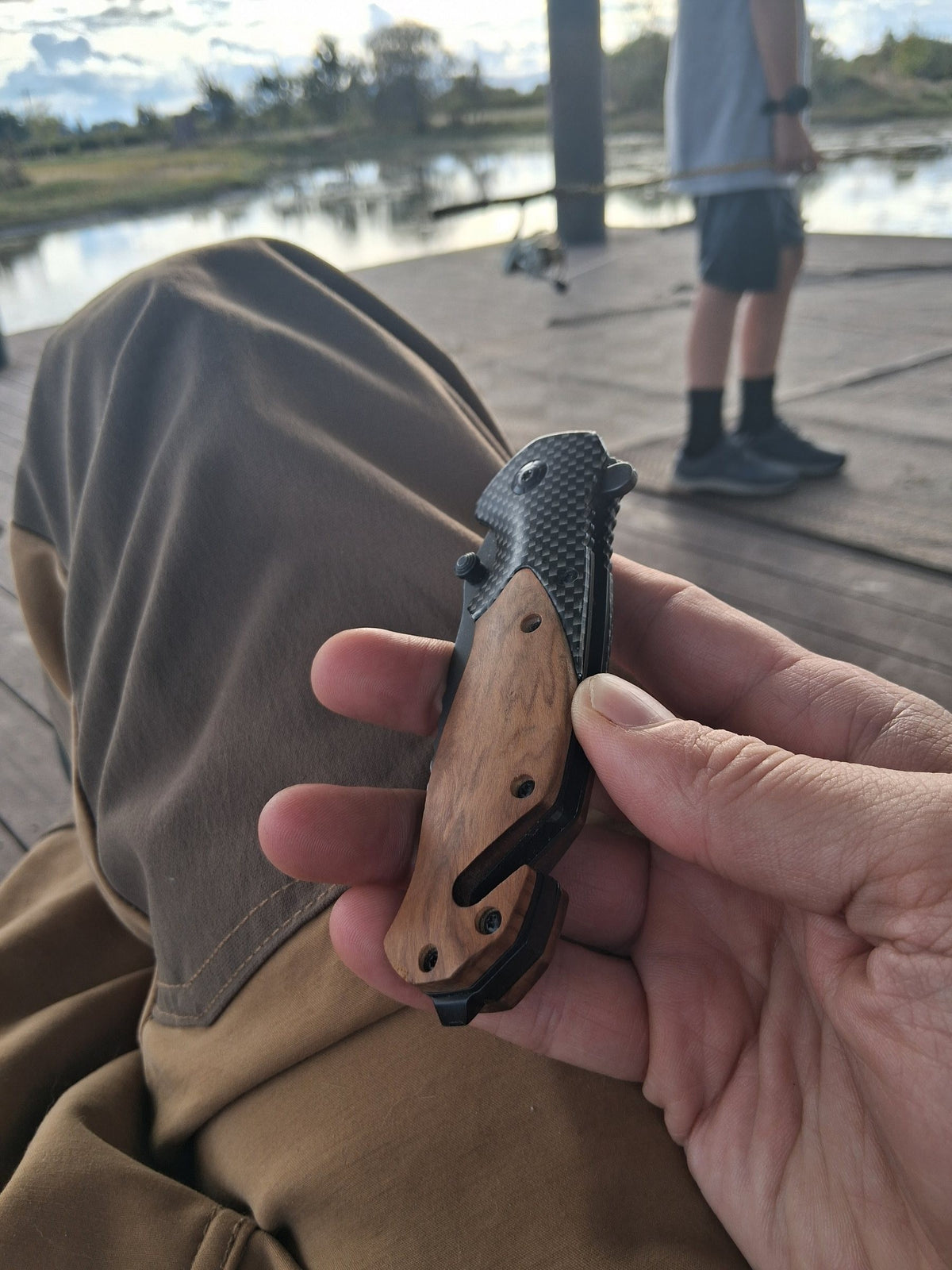 Hand holding a folded Ridgeblade pocket knife with a wood handle on a fishing dock