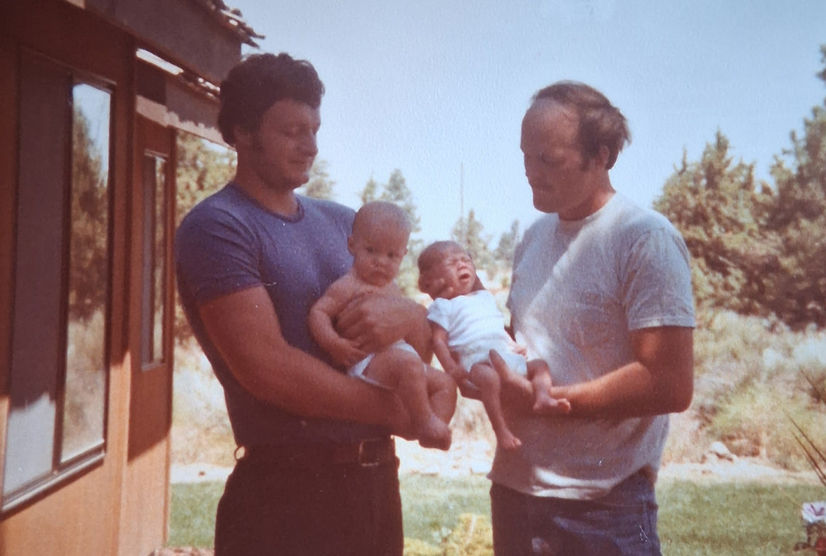 Vintage photo of the founder's father and his brother each holding a baby outside a cabin