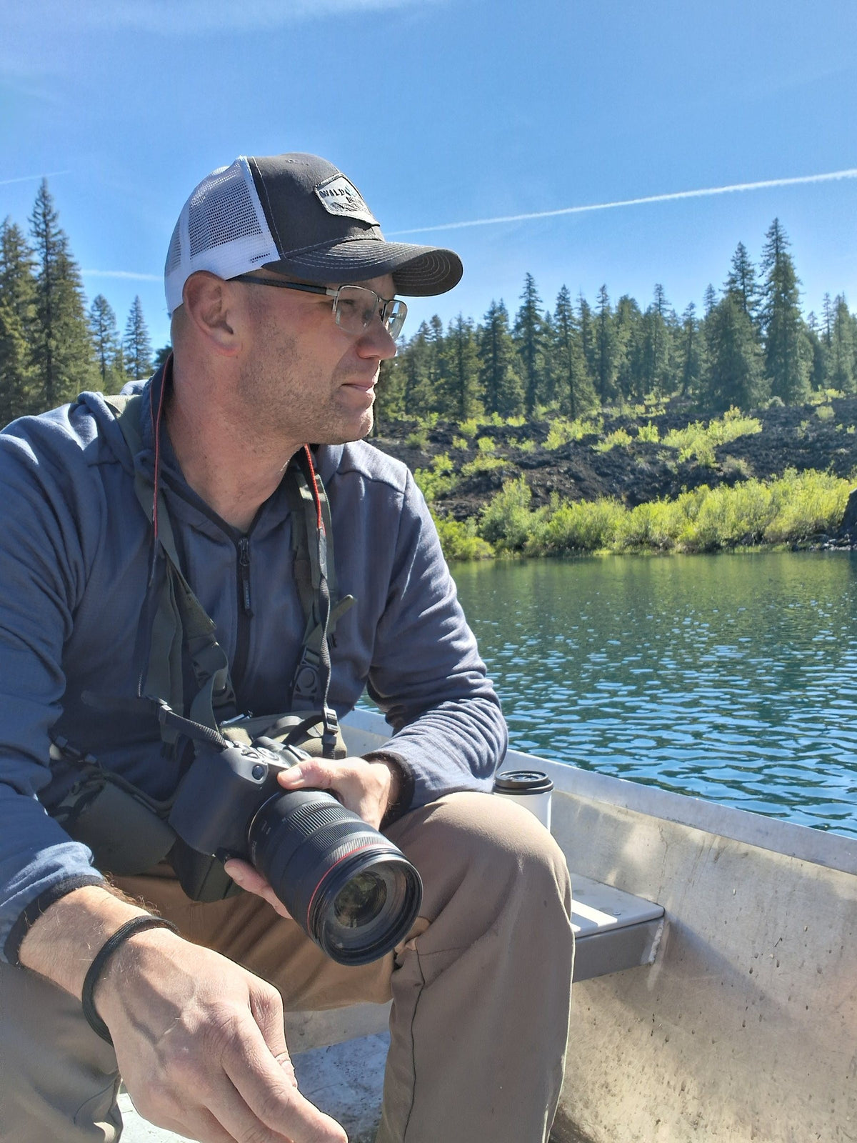 Founder sitting in an aluminum boat on a mountain lake with a camera