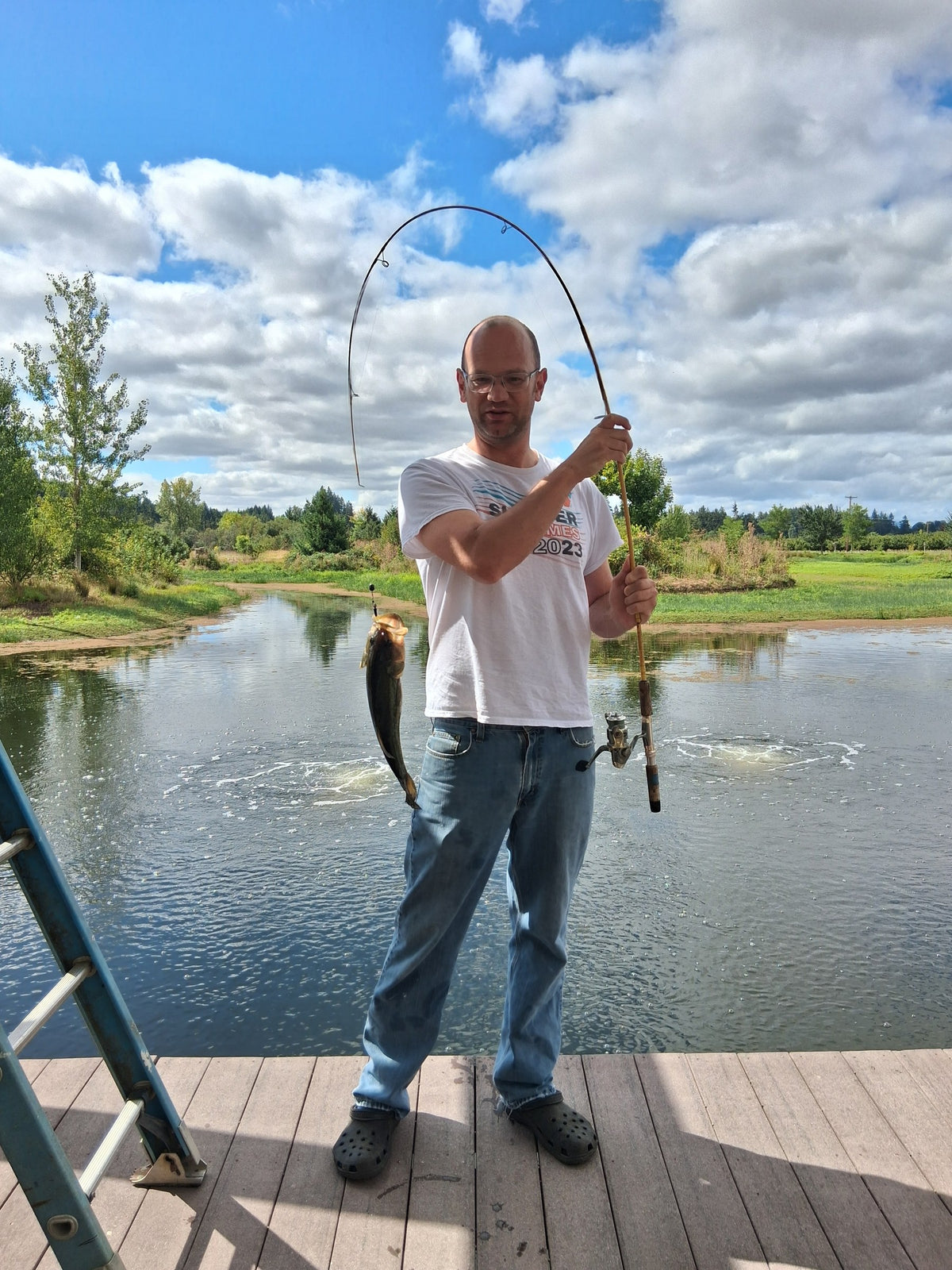 Founder holding up a fish on a bent rod at a pond dock